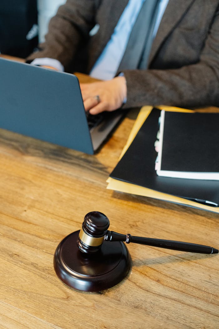 who-we-are From above of crop anonymous male lawyer in formal clothes typing on laptop while sitting at wooden table with stack of documents and gavel